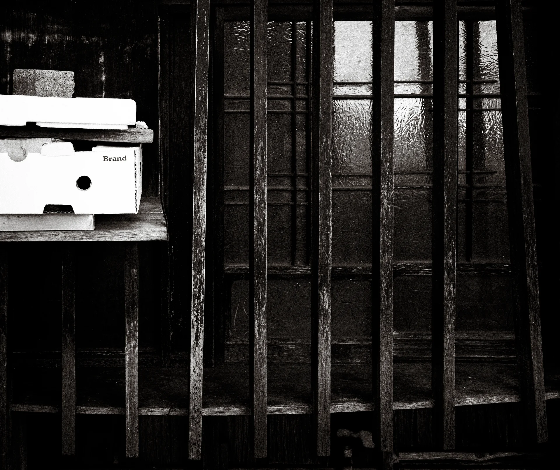 A pale mailbox sits beside dark wooden latticework covering textured glass doors in black and white.