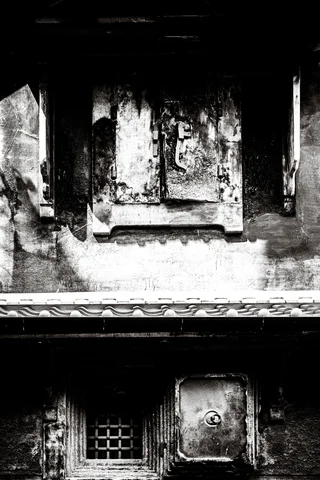 Weathered stone relief panels and small lower openings fill a heavily stained wall in black and white.