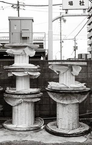 Large wooden cable reels stand stacked beside a block wall, with torn wrapping around their centers.