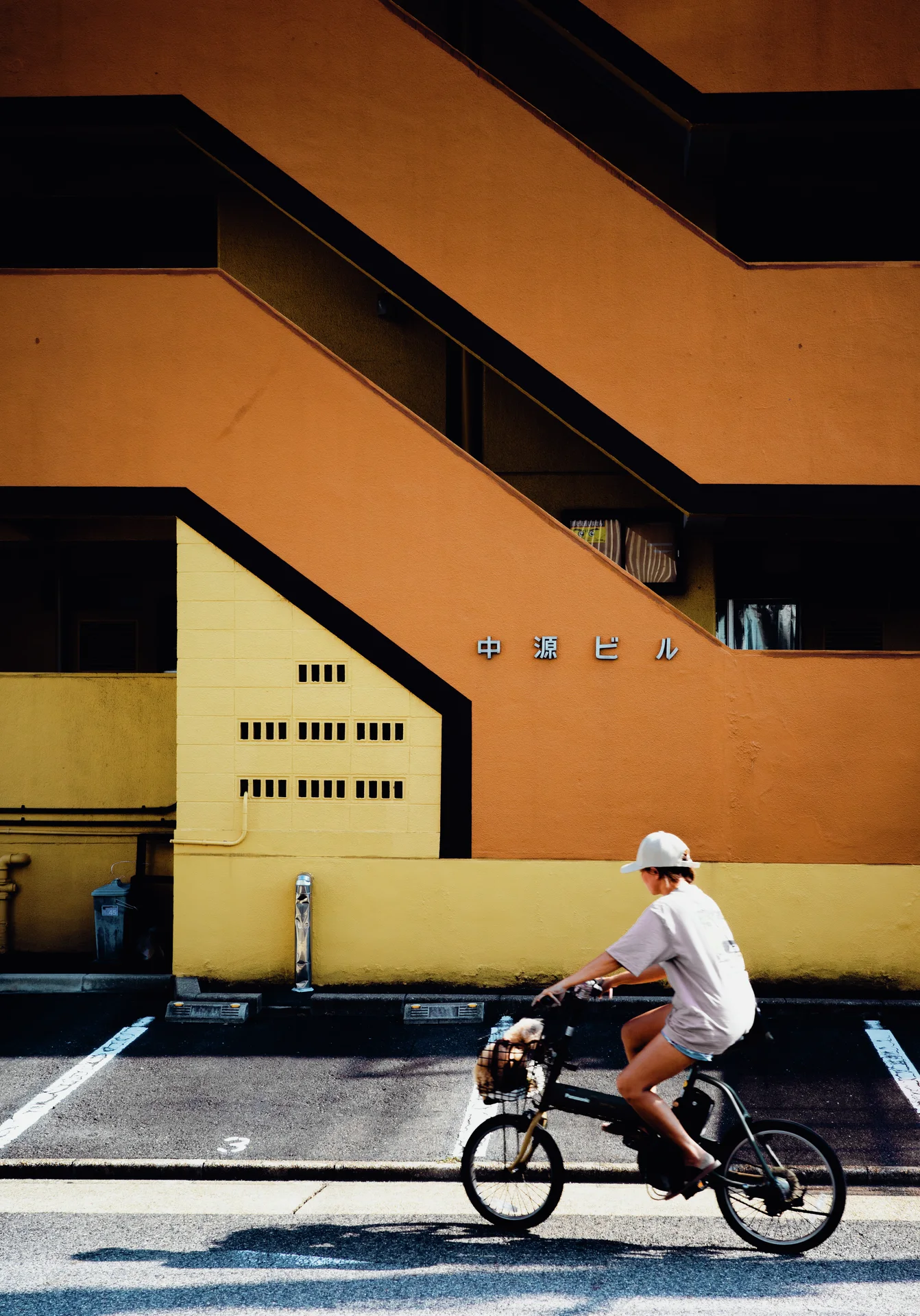 A cyclist passes an orange and yellow building with bold zigzagging exterior stair walls.