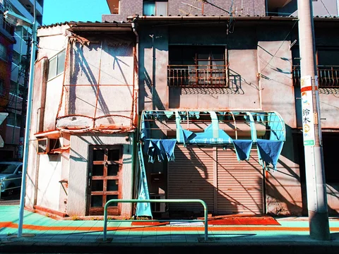 Torn blue awning strips hang over closed shutters on a weathered two-story storefront.