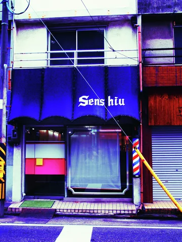 A blue salon awning shades glass doors beside a striped barber pole.