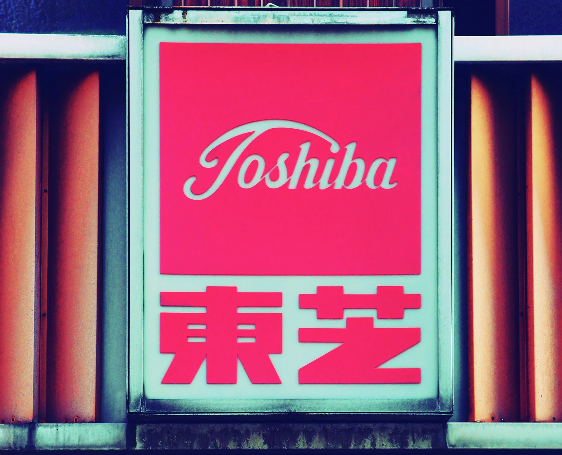 A pale-framed Toshiba sign combines a pink script panel and bold red Japanese characters.