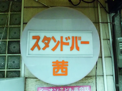 Orange Japanese characters decorate a large pale circular sign beside glass blocks and exposed cables.