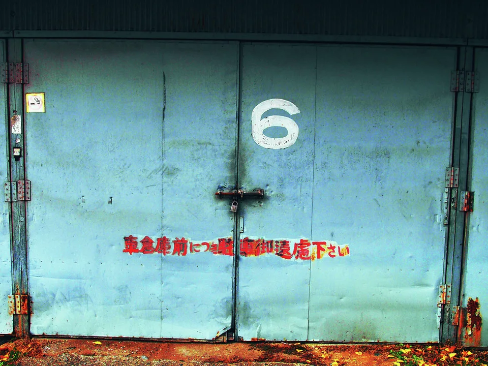 A white numeral six marks locked turquoise double doors with red Japanese lettering and rusty lower edges.