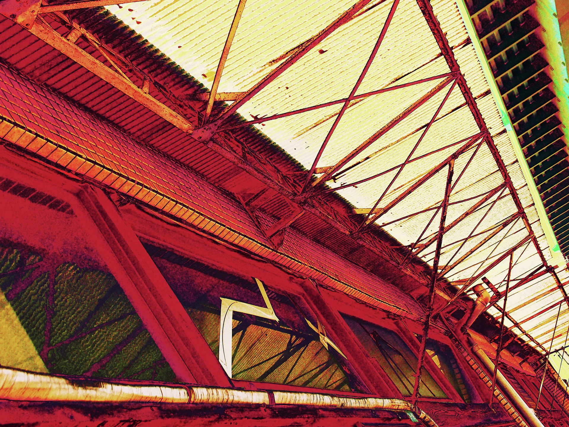 Red steel beams support pale translucent roof panels above a weathered industrial interior viewed upward.