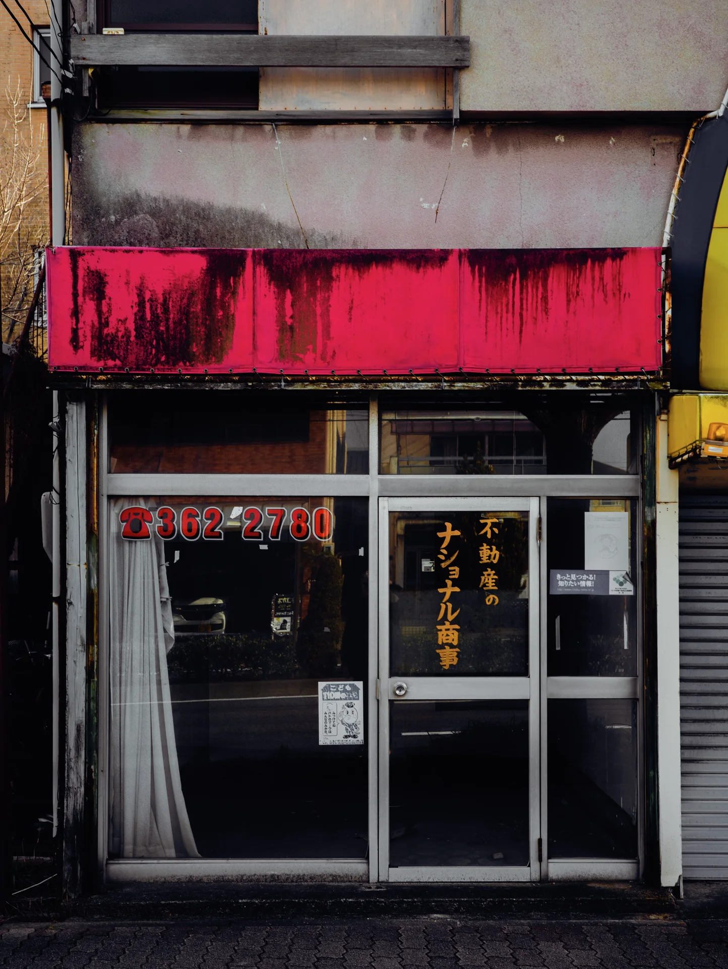 A stained bright pink fascia hangs above dark glass storefront doors with small Japanese lettering.
