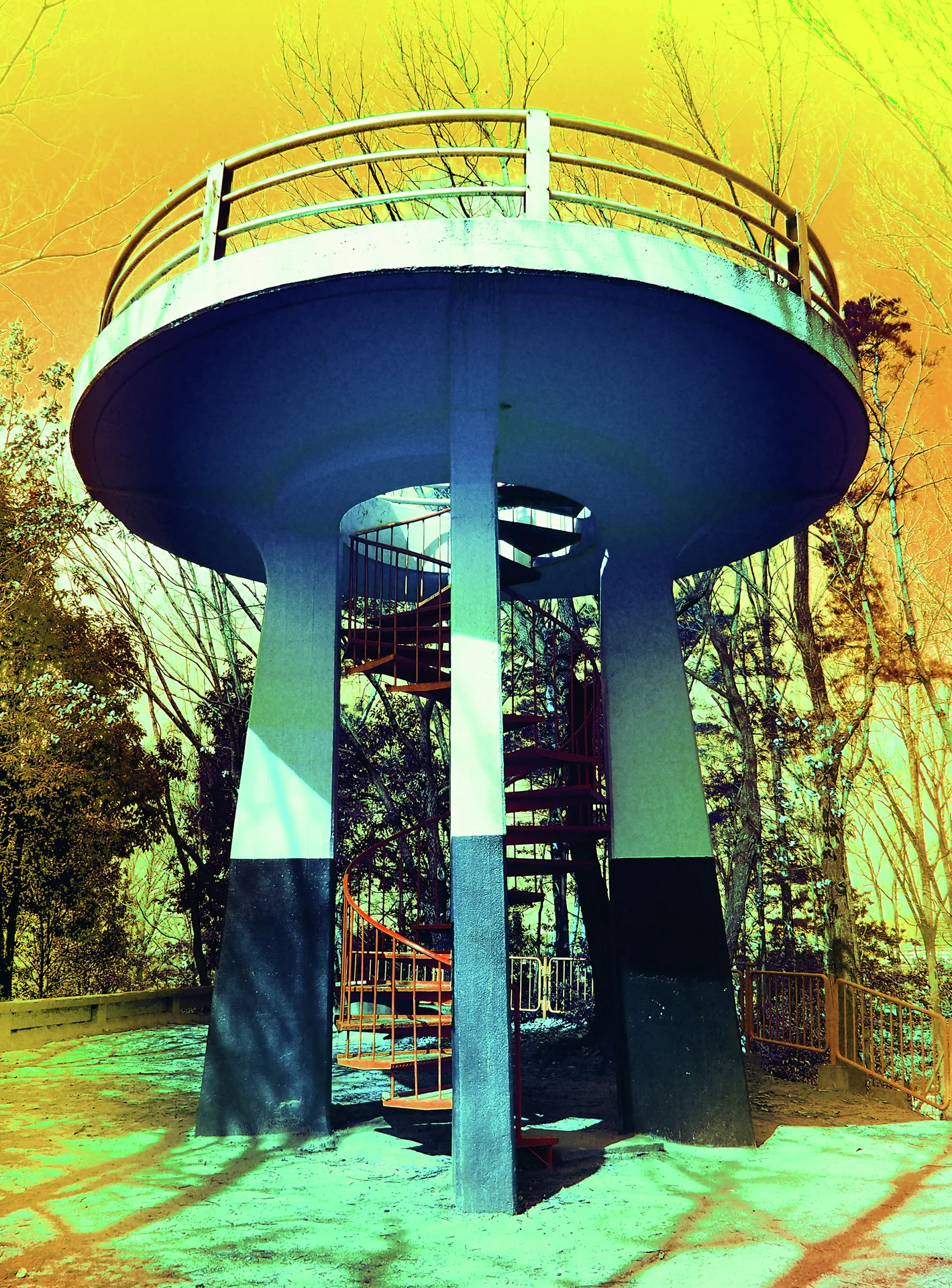 A circular elevated platform with railings rests on blue supports around a spiral staircase among trees.