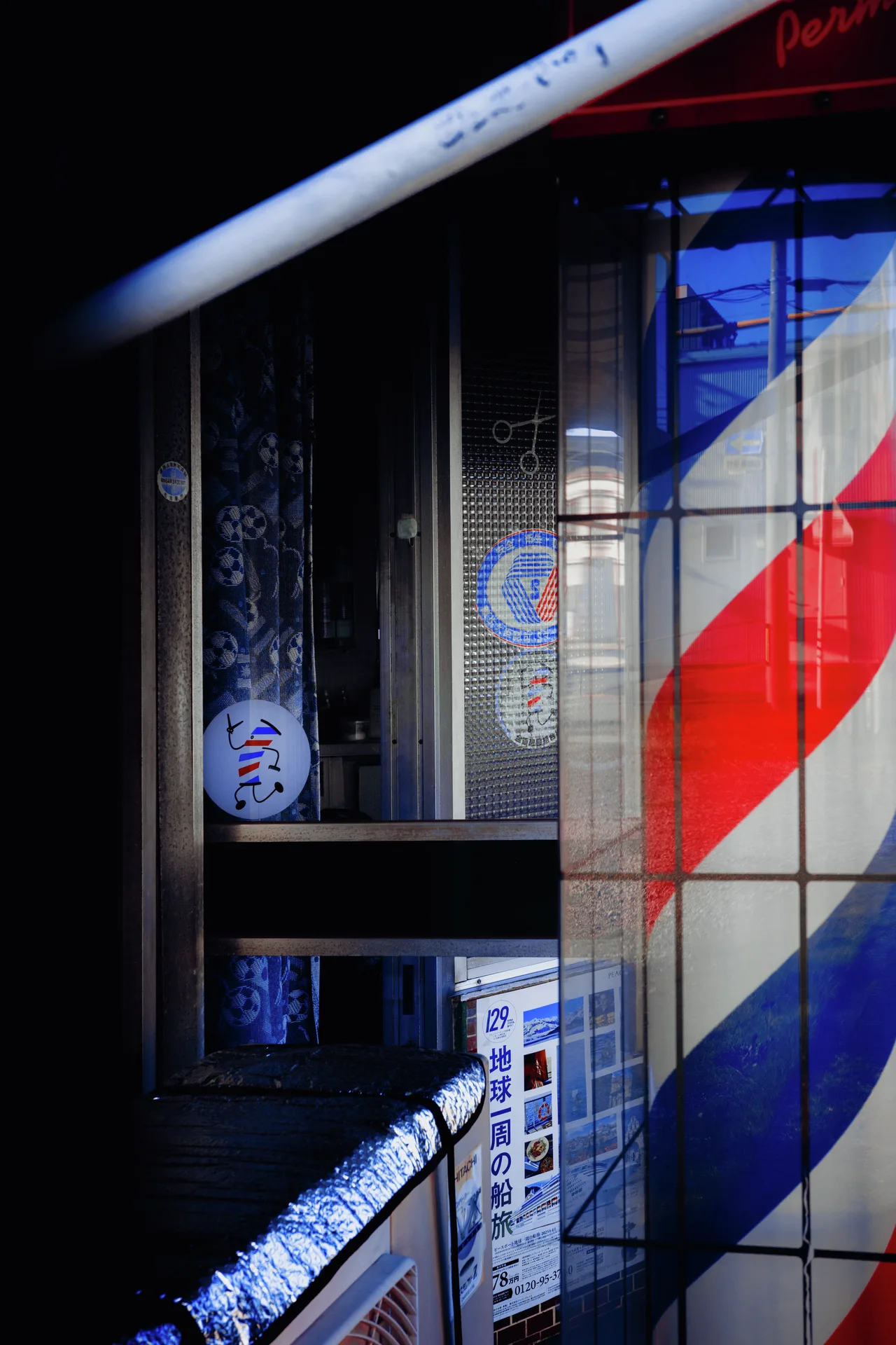 Red, white, and blue diagonal stripes mark a tiled storefront pillar beside a dark glass entrance.