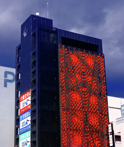 A dark tower features a tall red patterned panel and stacked signs beneath gray clouds.