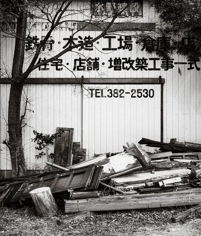 Discarded wooden boards and frames lie beneath bold wall lettering and bare branches in black and white.