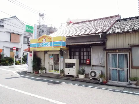 A yellow-and-blue shop canopy adjoins a tiled-roof house with barred windows and outdoor air-conditioning units.