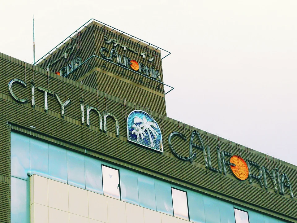 Raised City Inn California lettering and a palm-tree emblem span a dark tiled building facade.