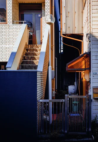 A sunlit exterior staircase rises beside a narrow passage and a small orange canopy.