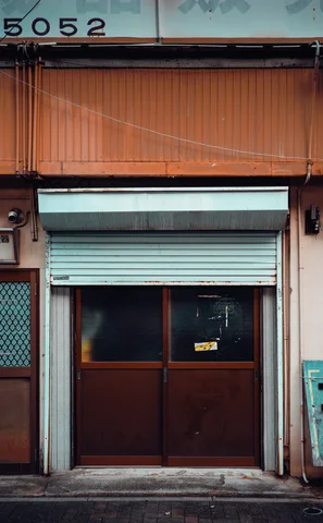 An orange awning hangs over a partially lowered blue shutter and dark double doors.