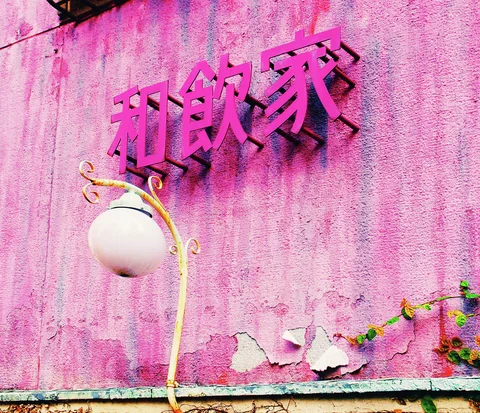 Raised pink Japanese characters hang above a white globe lamp on a peeling pink wall.