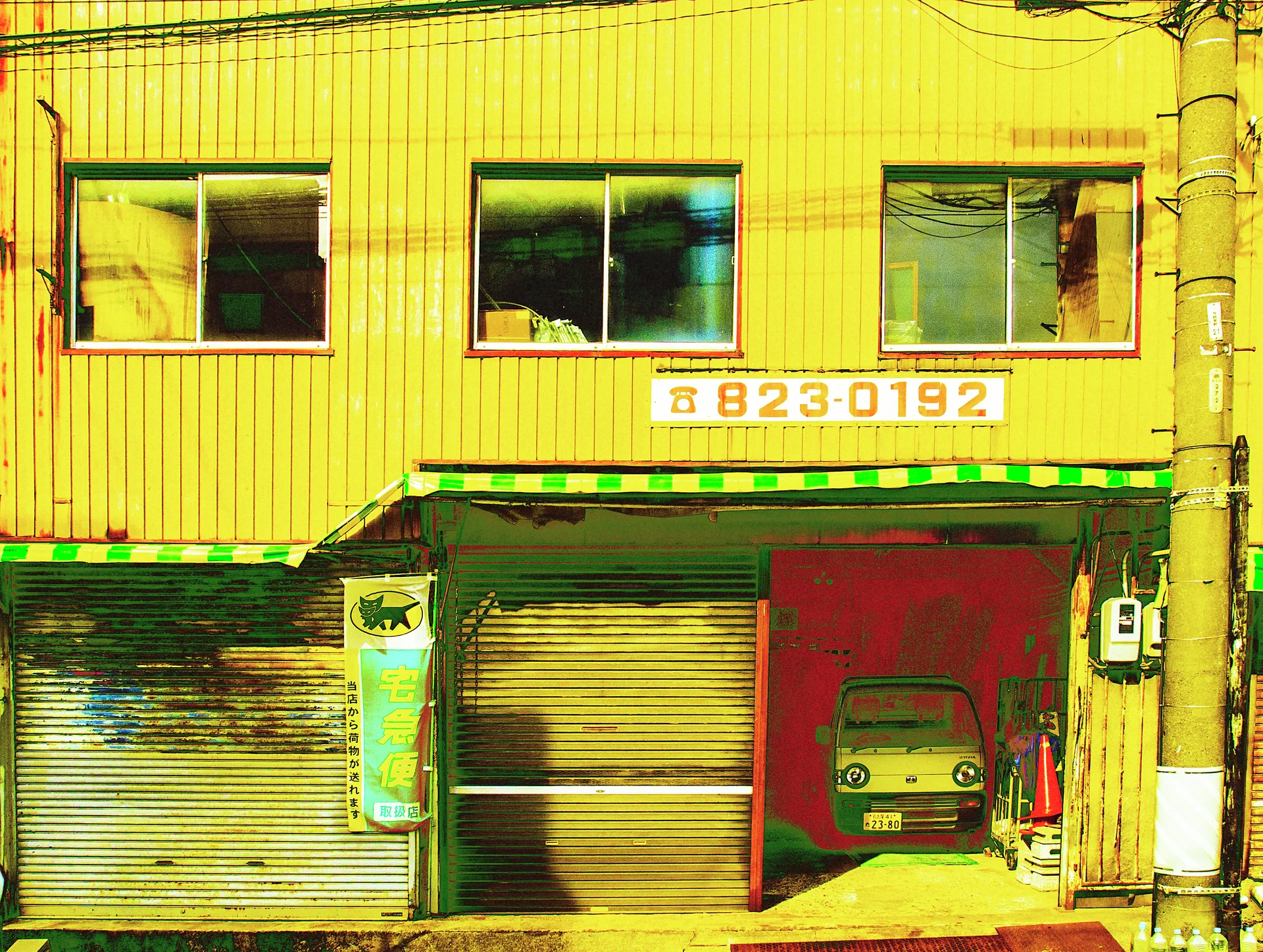 A small car sits behind a partly raised shutter beneath yellow corrugated siding and three upper windows.