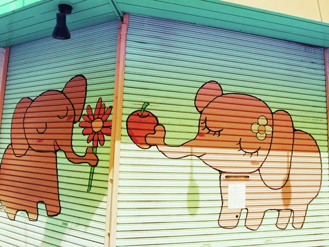 Cartoon elephants holding a flower and an apple decorate pale green corner shutters.