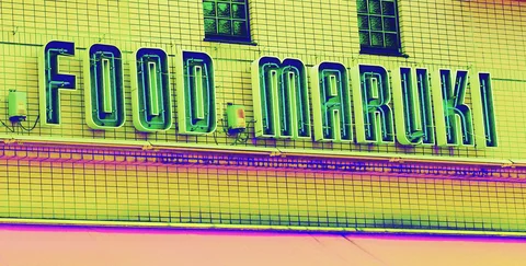 Tall blue outlined letters span a yellow tiled facade beneath two small dark windows.