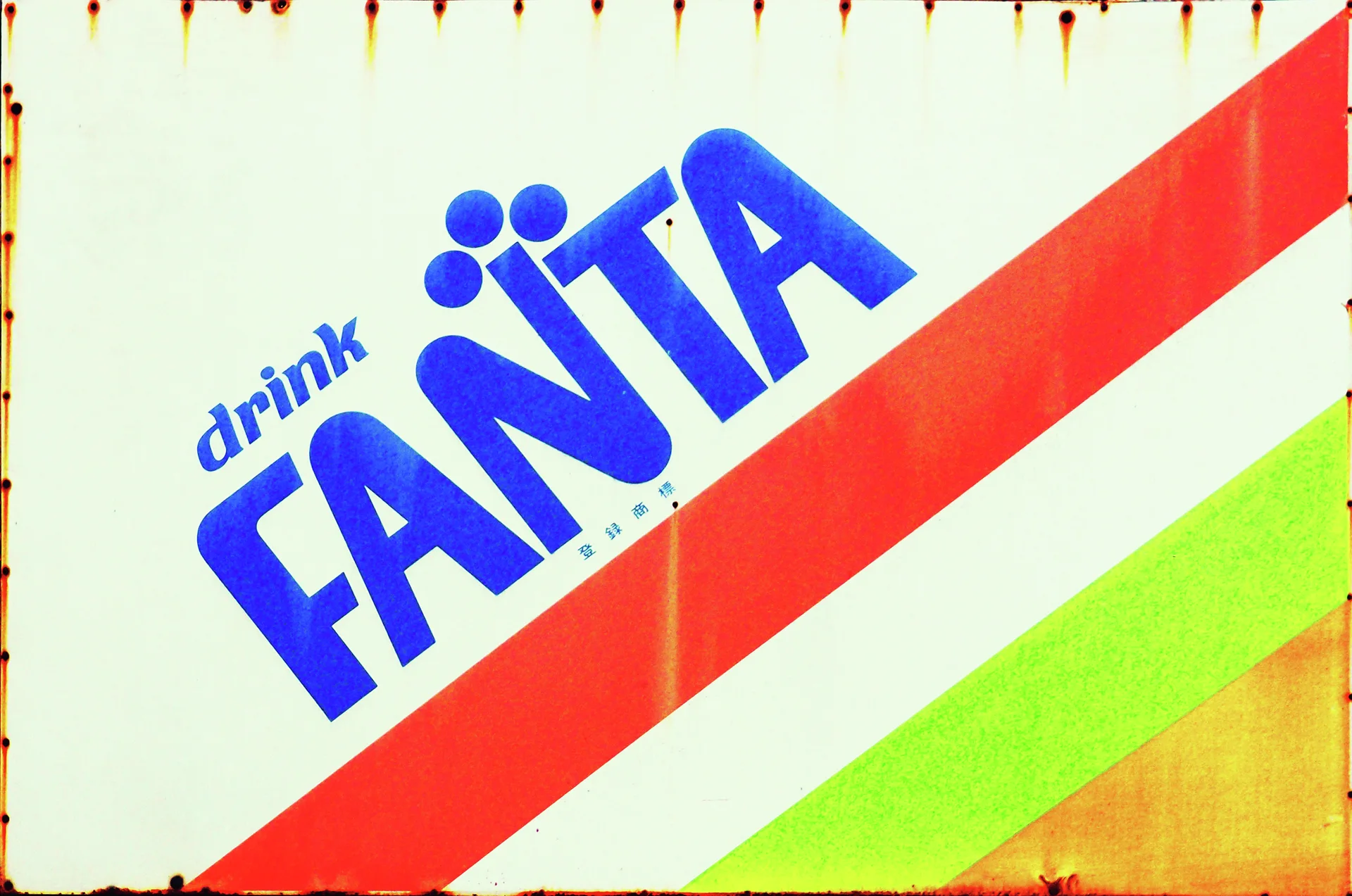 Blue FANTA lettering sits above diagonal red, green, and orange stripes on a weathered white sign.