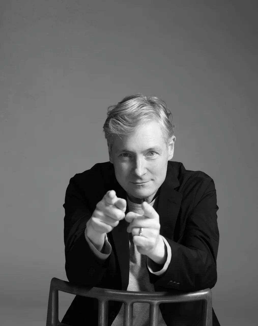 Ray Larabie seated behind a chair, pointing toward the camera.