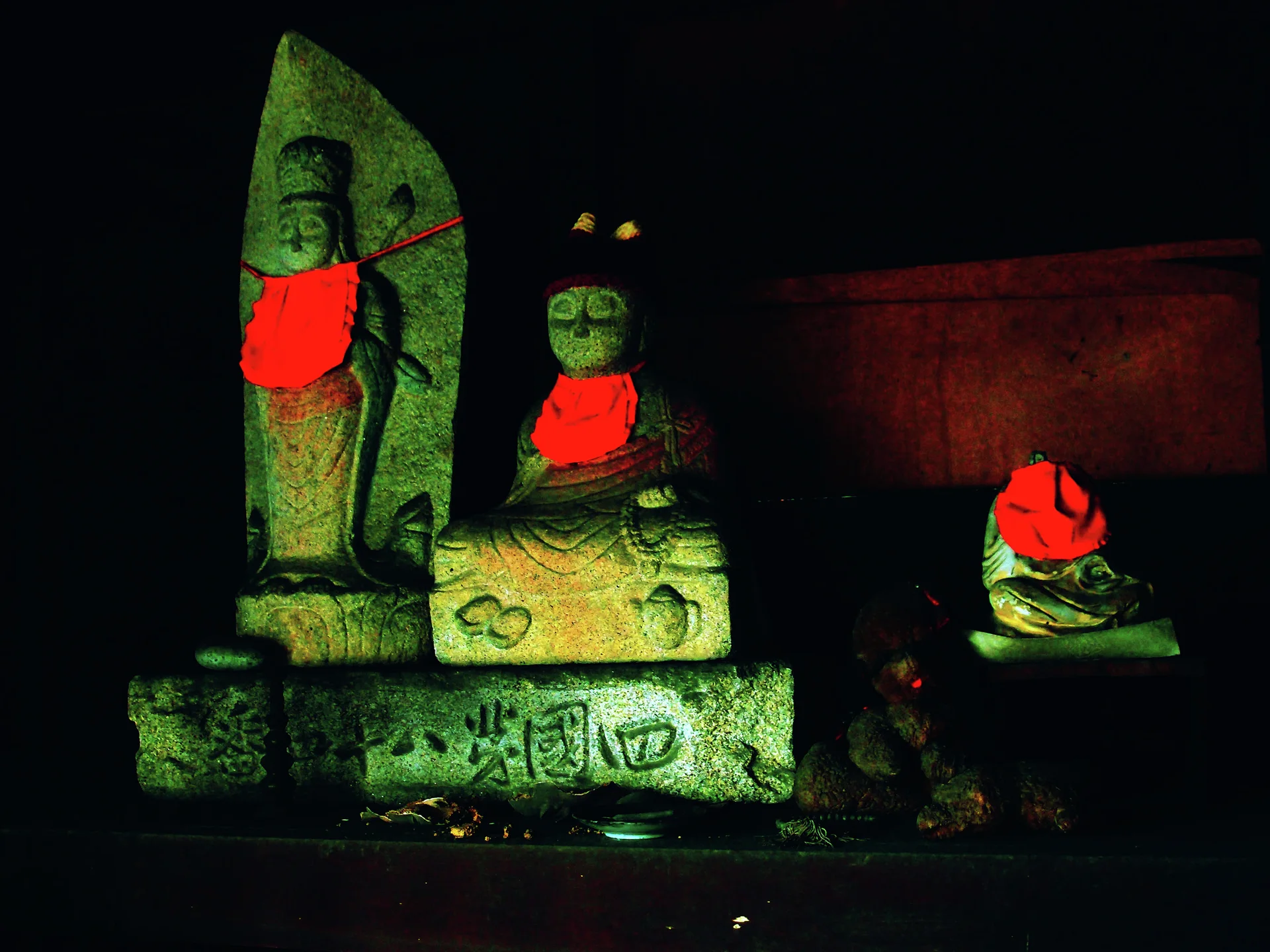 Three stone religious figures wear bright red cloths against a dark wooden background.
