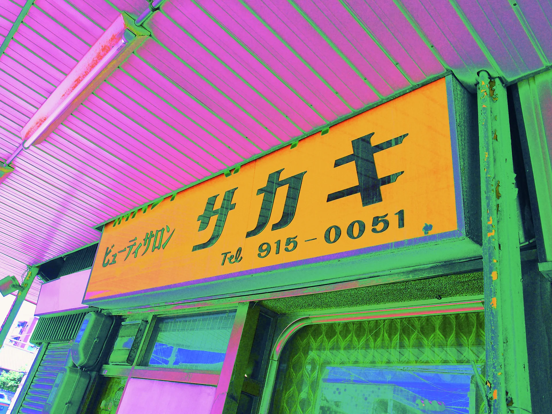 A yellow hair salon sign with dark Japanese lettering hangs beneath a pink corrugated canopy.