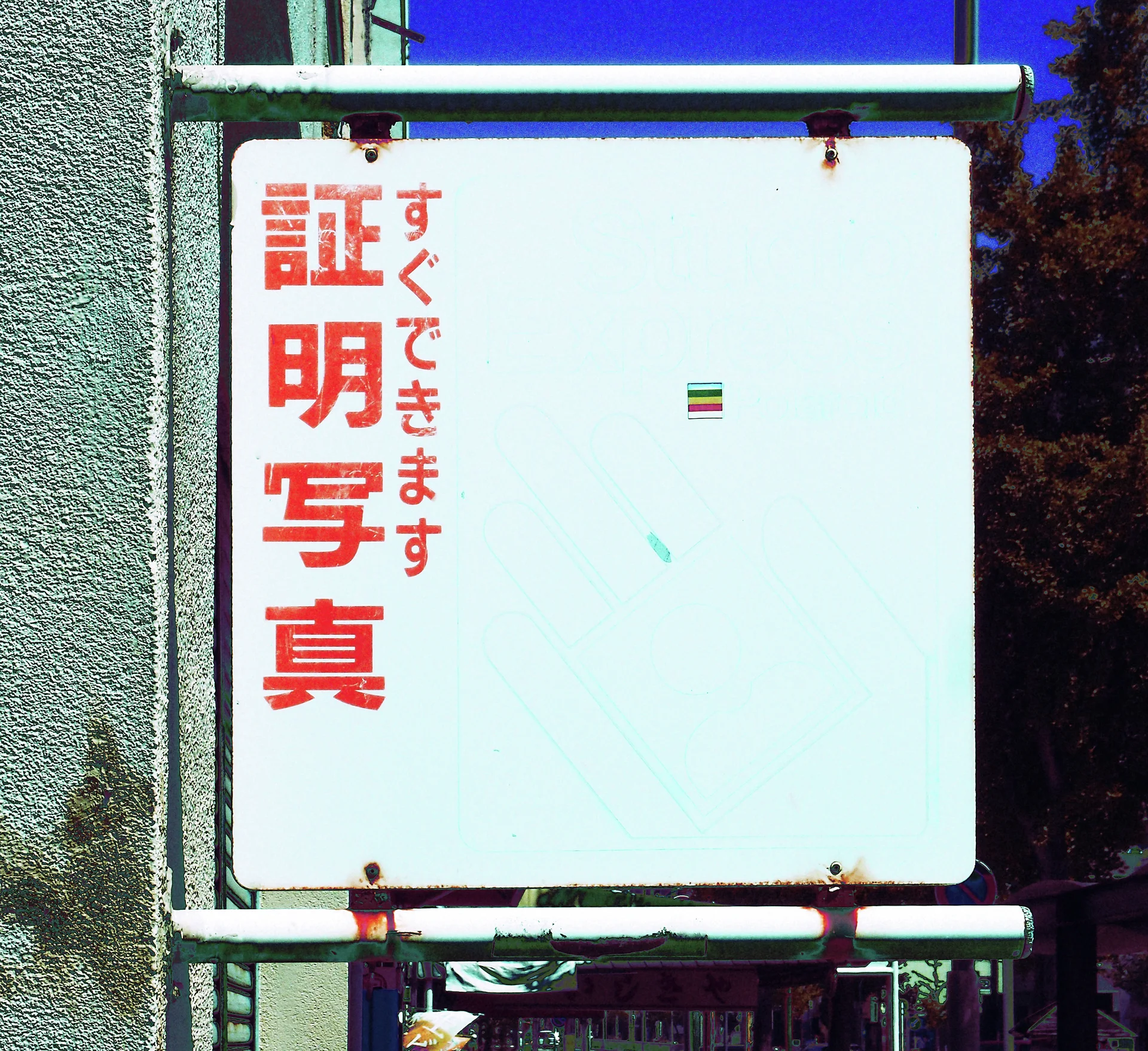 Red Japanese lettering occupies one side of a mostly blank pale sign within rust-stained metal supports.