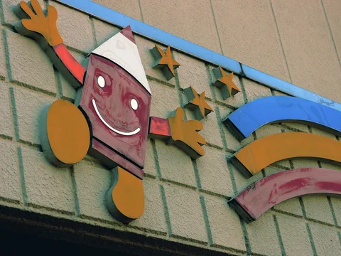 A smiling red figure with yellow hands and feet stretches beside stars and rainbow bands on a wall.