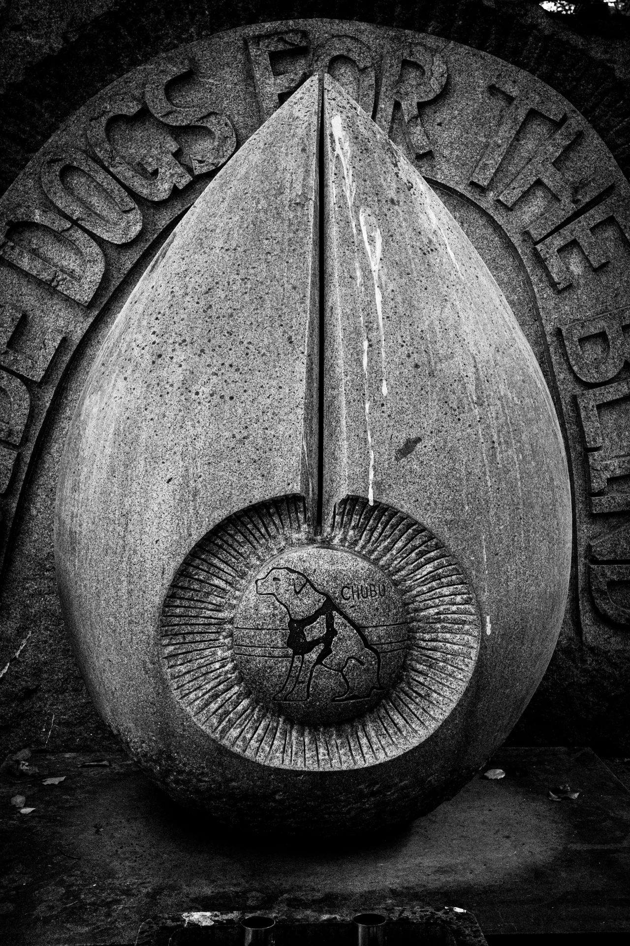 A carved pointed oval ornament with a circular center rests against inscribed stone in black and white.
