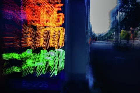 Blurred orange and green illuminated numbers glow beside a dark blue window reflecting the street.
