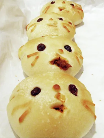 Four pale round buns with dark eyes and small facial details form a row on white paper.