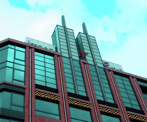 Two pointed vertical towers crown a turquoise-windowed building divided by reddish columns and gold geometric trim.