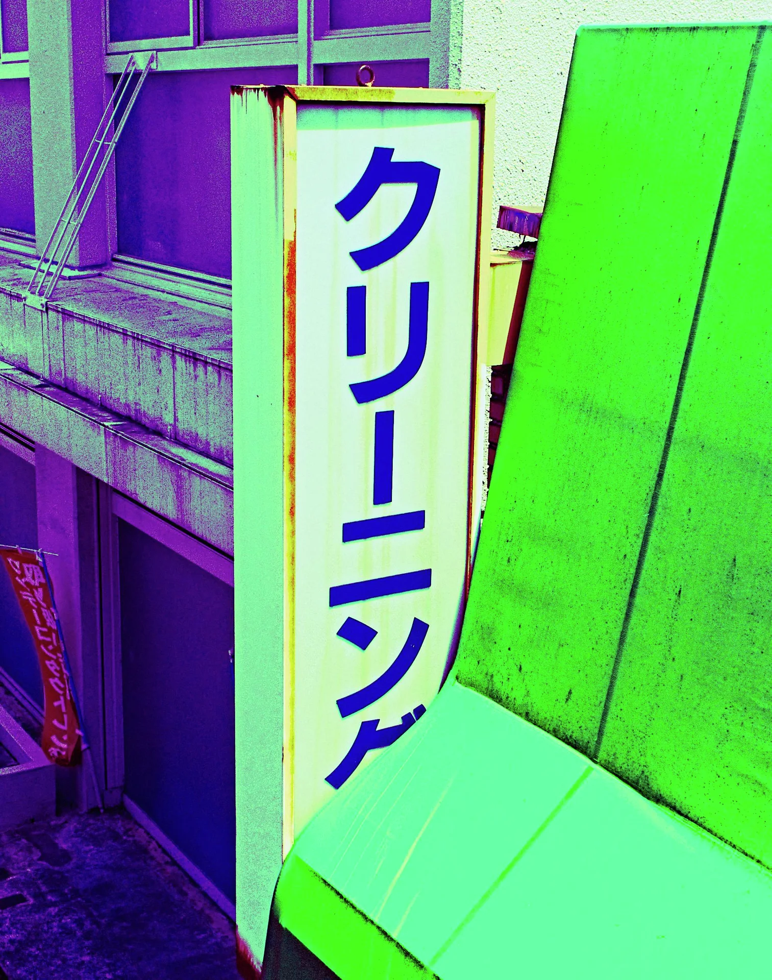 Bold blue Japanese characters run vertically down a pale sign beside a bright green awning.