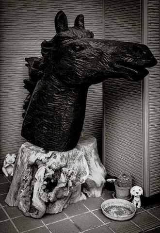 A dark sculpted horse head rests on a rough pale base beside small bowls in black and white.