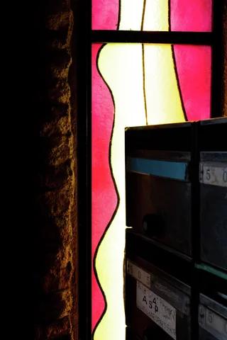 Red and yellow stained glass glows behind a dark foreground cabinet with rectangular compartments.