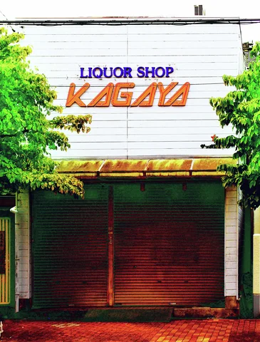 A liquor shop sign sits above a closed dark shutter, framed by leafy trees and a yellow awning.