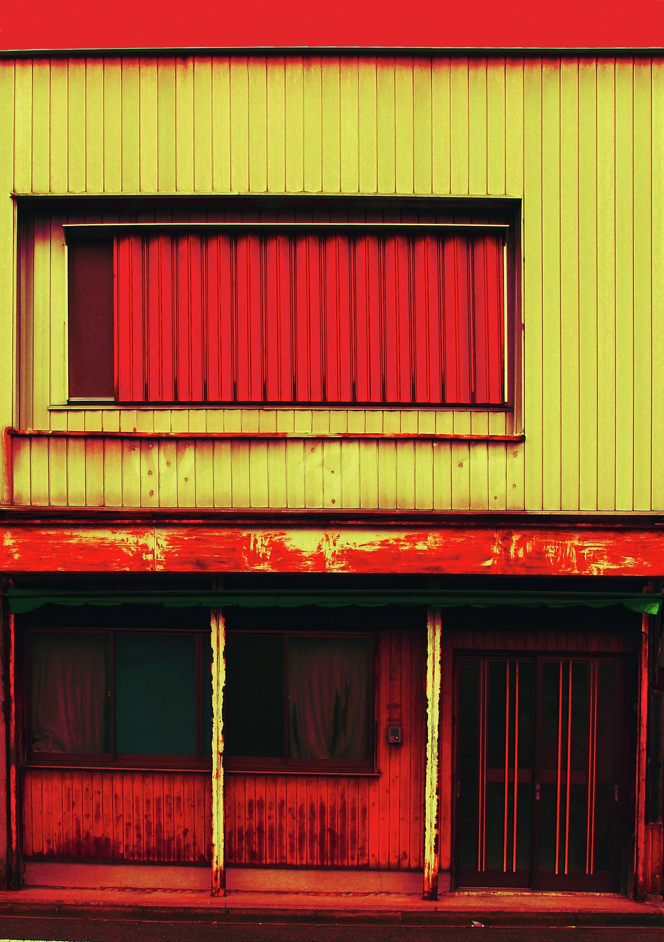 A red shutter sits above curtained windows and a sliding door on a yellow and red building facade.