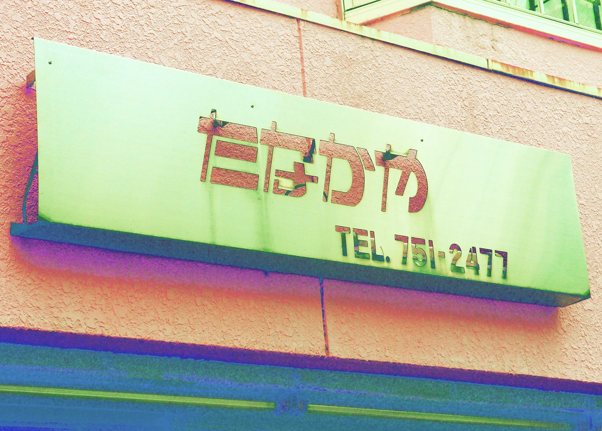 Raised red lettering and a telephone number mark a pale rectangular sign on a pink wall.