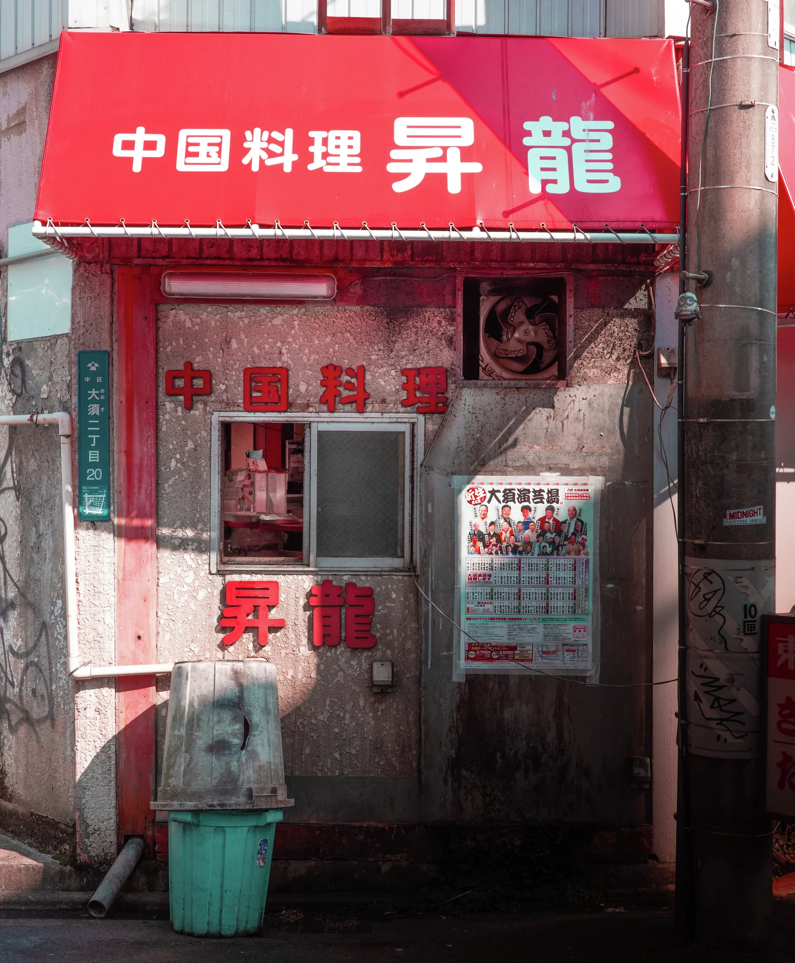 A narrow restaurant entrance has a bright red awning and lettering above its weathered glass door.