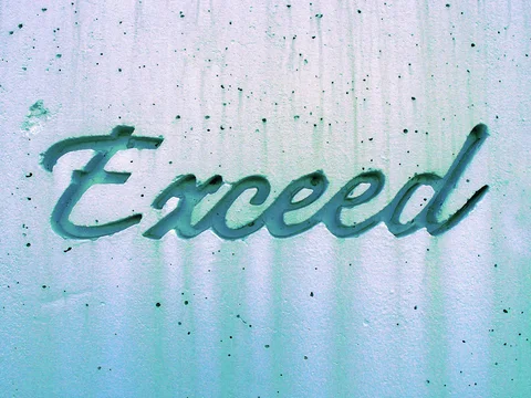 Green cursive Exceed lettering projects from a pale concrete wall dotted with small circular holes.