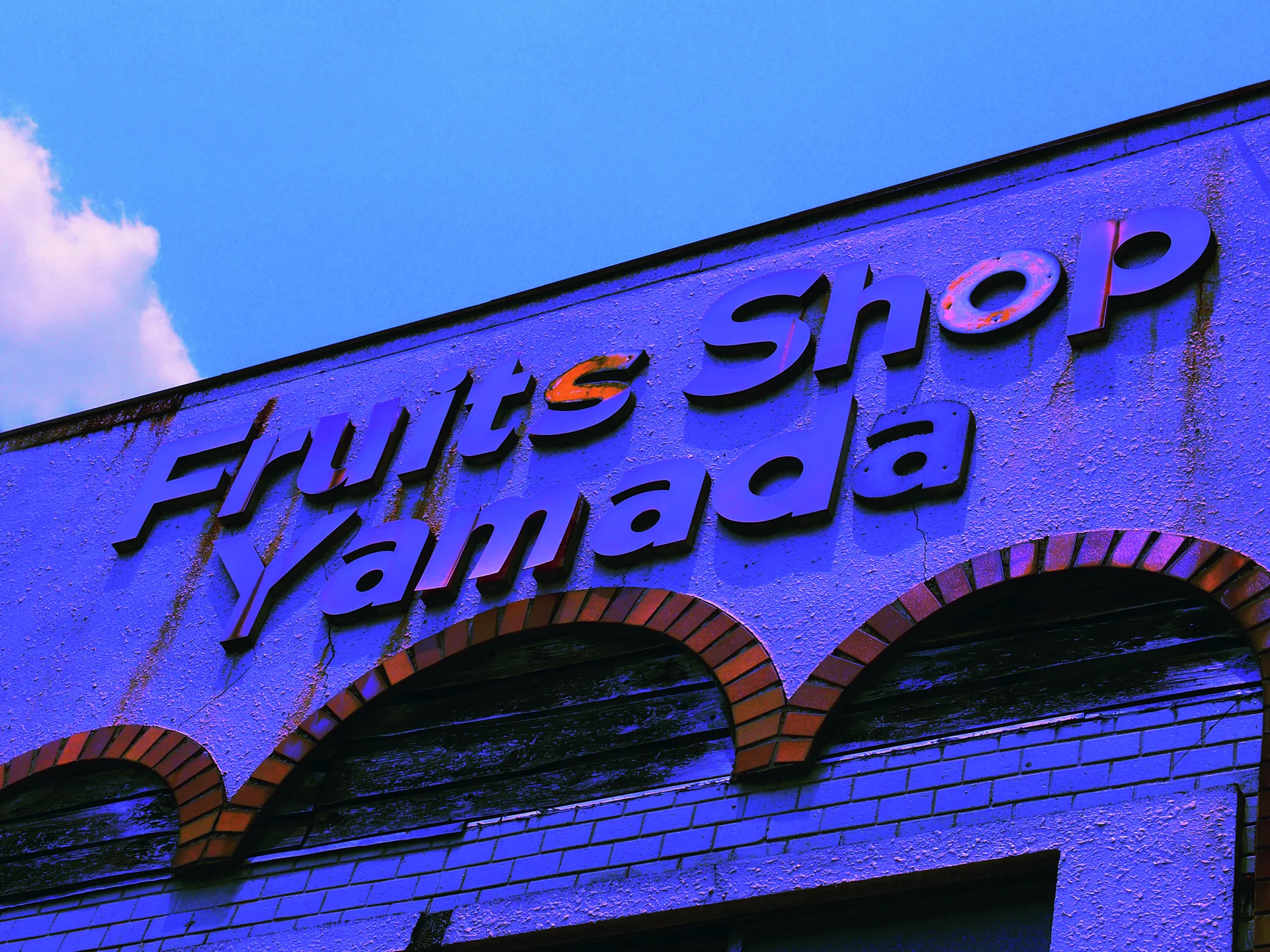 Raised lettering stretches across a blue-toned facade above three brick-trimmed arches under a clear sky.