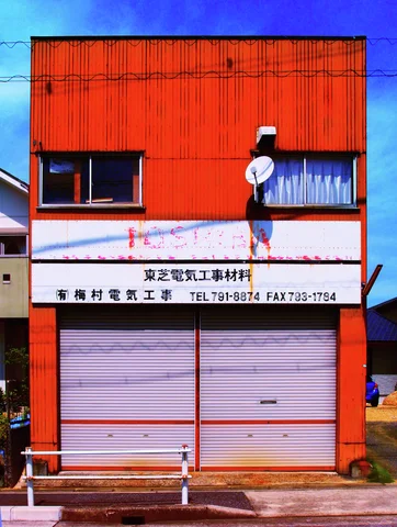 An orange two-story shop has dark upper windows above a broad pale sign and closed gray shutters.