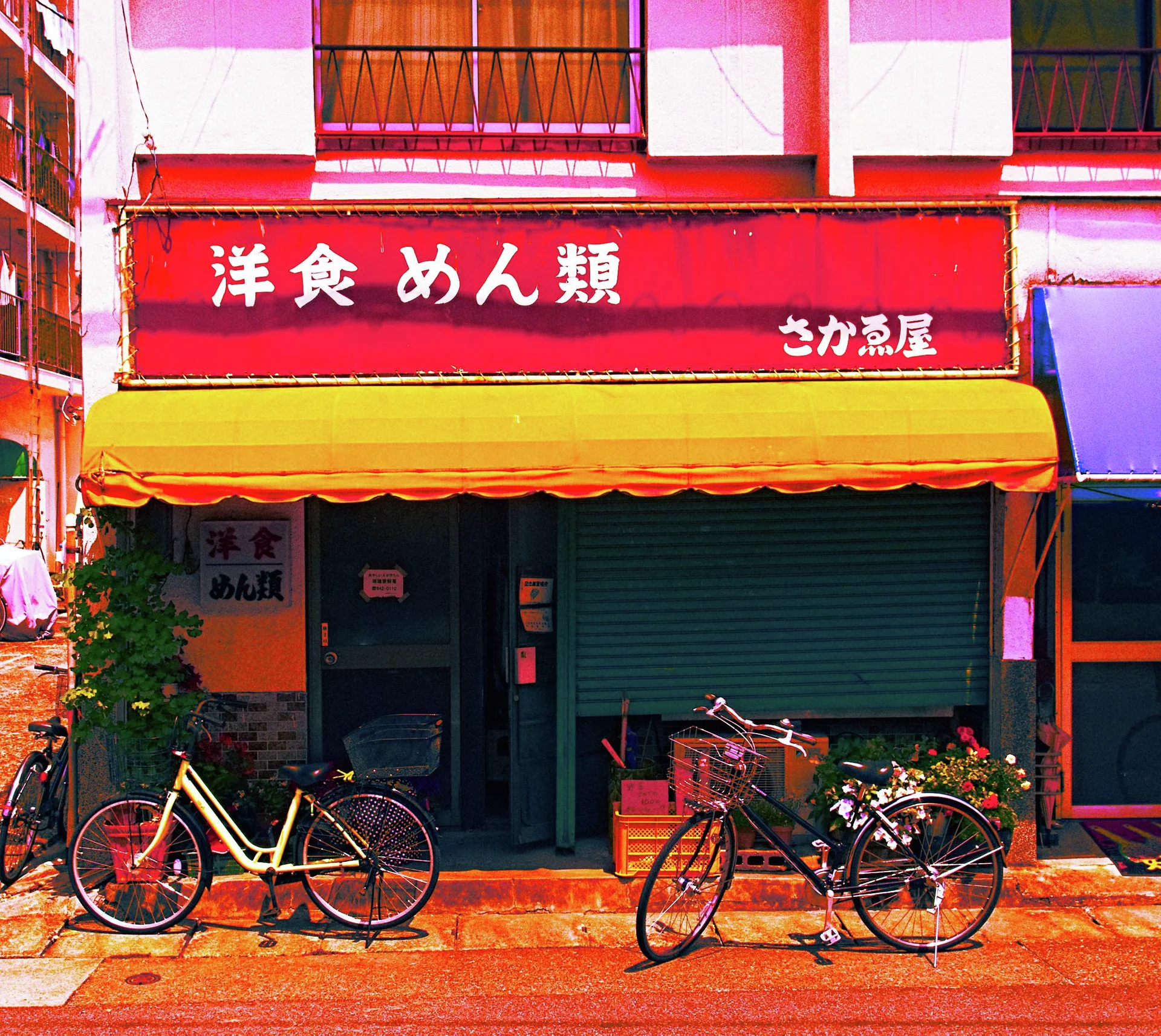 Bicycles stand outside a restaurant beneath a red sign and bright yellow awning.