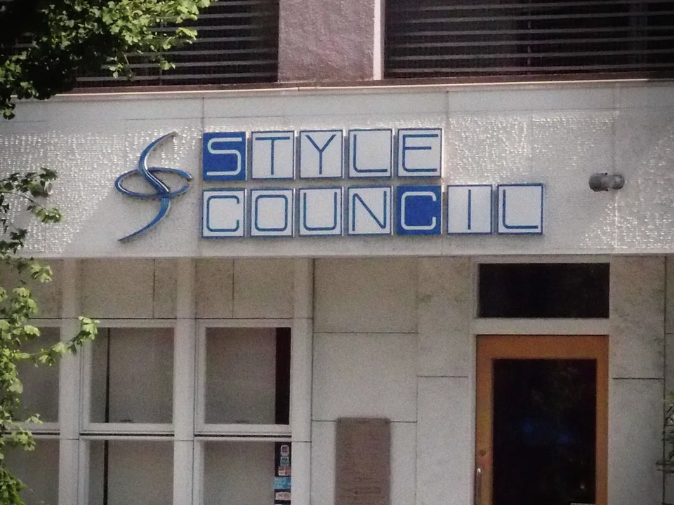 Blue outlined Style Council lettering marks a pale facade above windows and a narrow wooden-framed door.