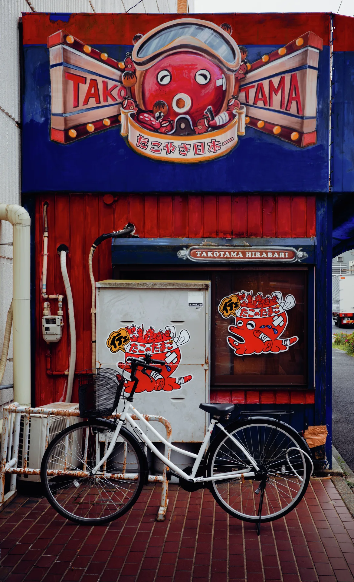 A white bicycle rests outside a red and blue storefront decorated with a cartoon octopus sign.