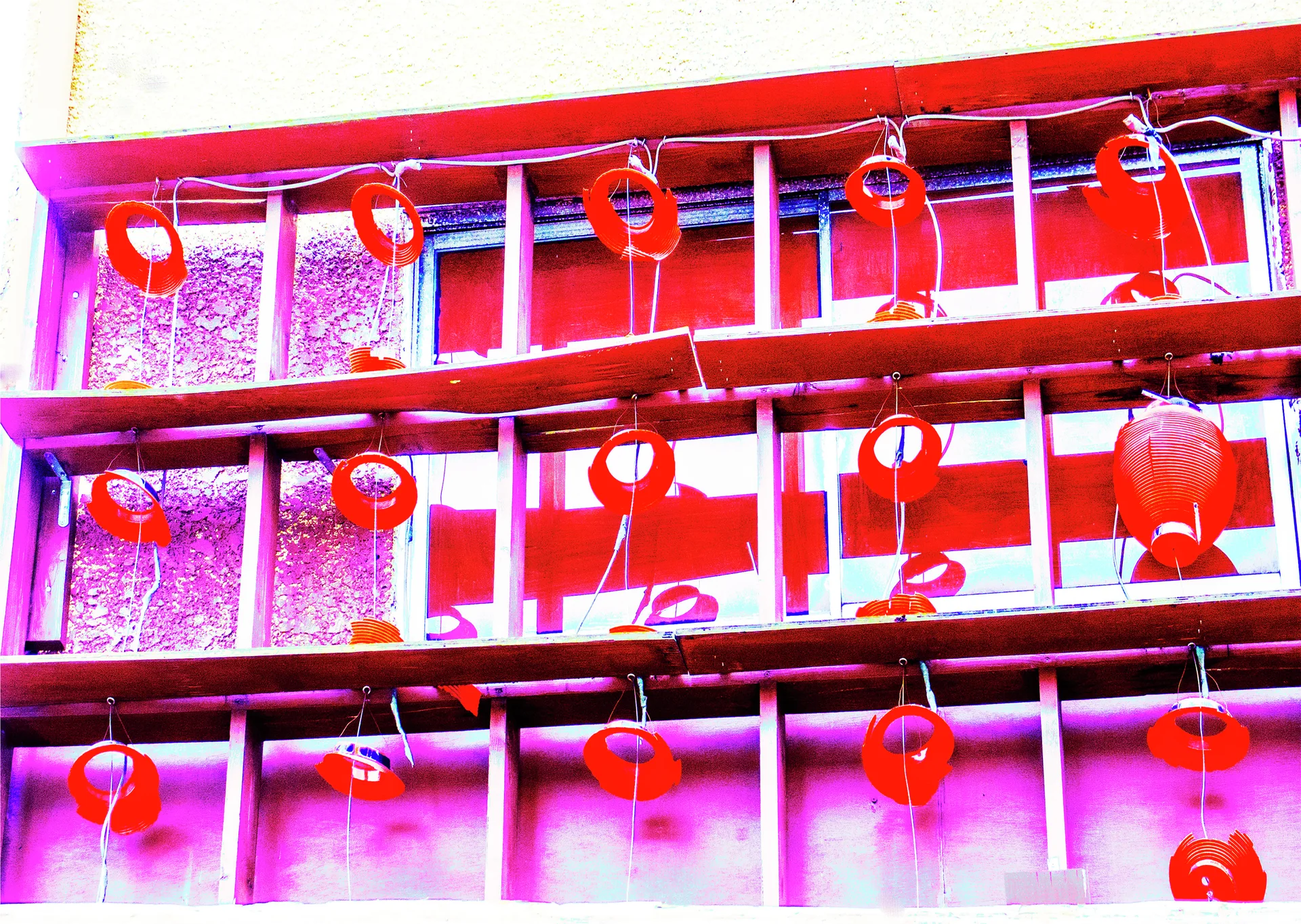 Rows of red hanging lanterns and circular ornaments decorate a gridded window with pink reflections.