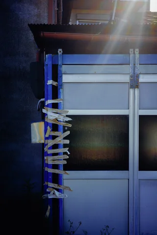Tape strips secure the edge of a pale paneled door beneath a shaft of sunlight.