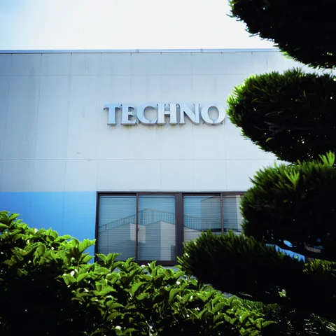 Raised silver lettering marks a pale blue building facade partly obscured by neatly trimmed trees and shrubs.