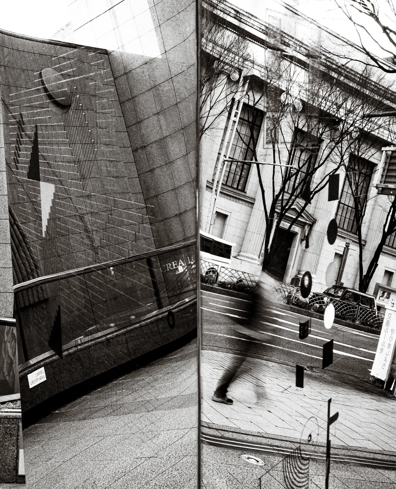 A reflective panel juxtaposes buildings, bare branches and a blurred passerby in black and white.